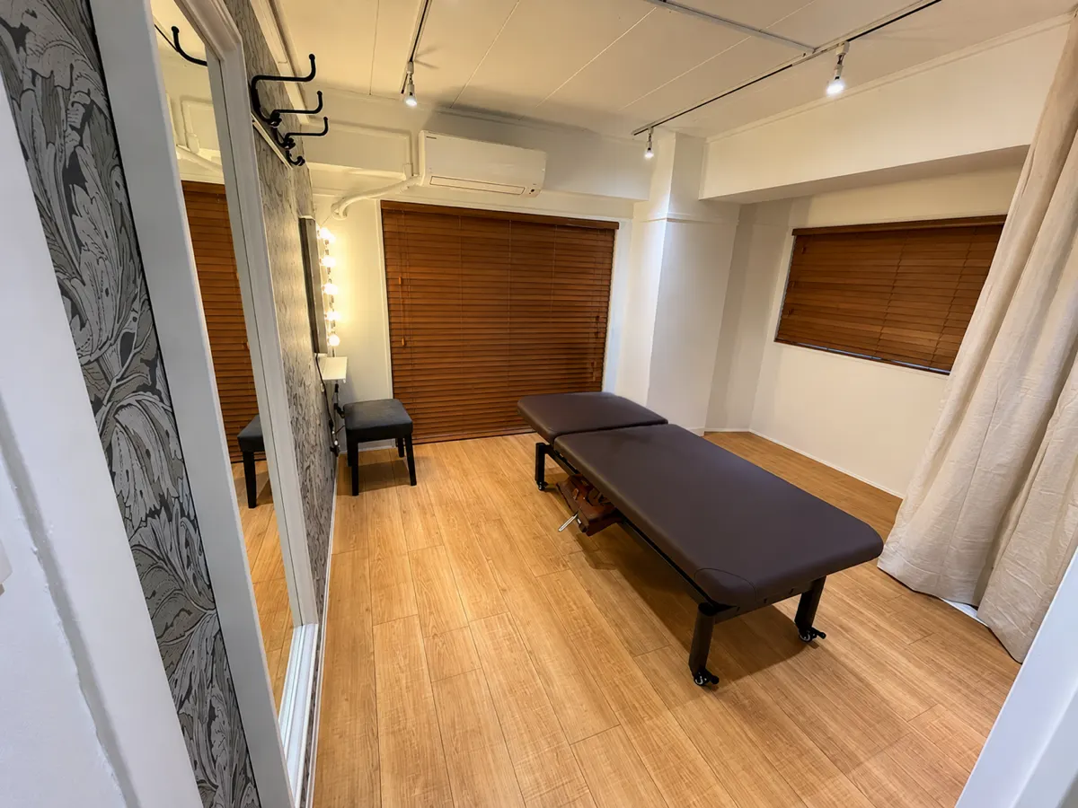 池袋店の施術室（施術ベッドと木目の床の明るい個室）